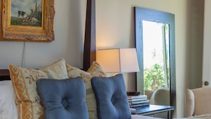Habitación de hotel con cama, almohadas, lámpara, una silla y un cuadro en la pared.