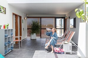 A person sitting on a lounge chair in a modern indoor space with a potted plant, a water bottle, and a towel on the floor.