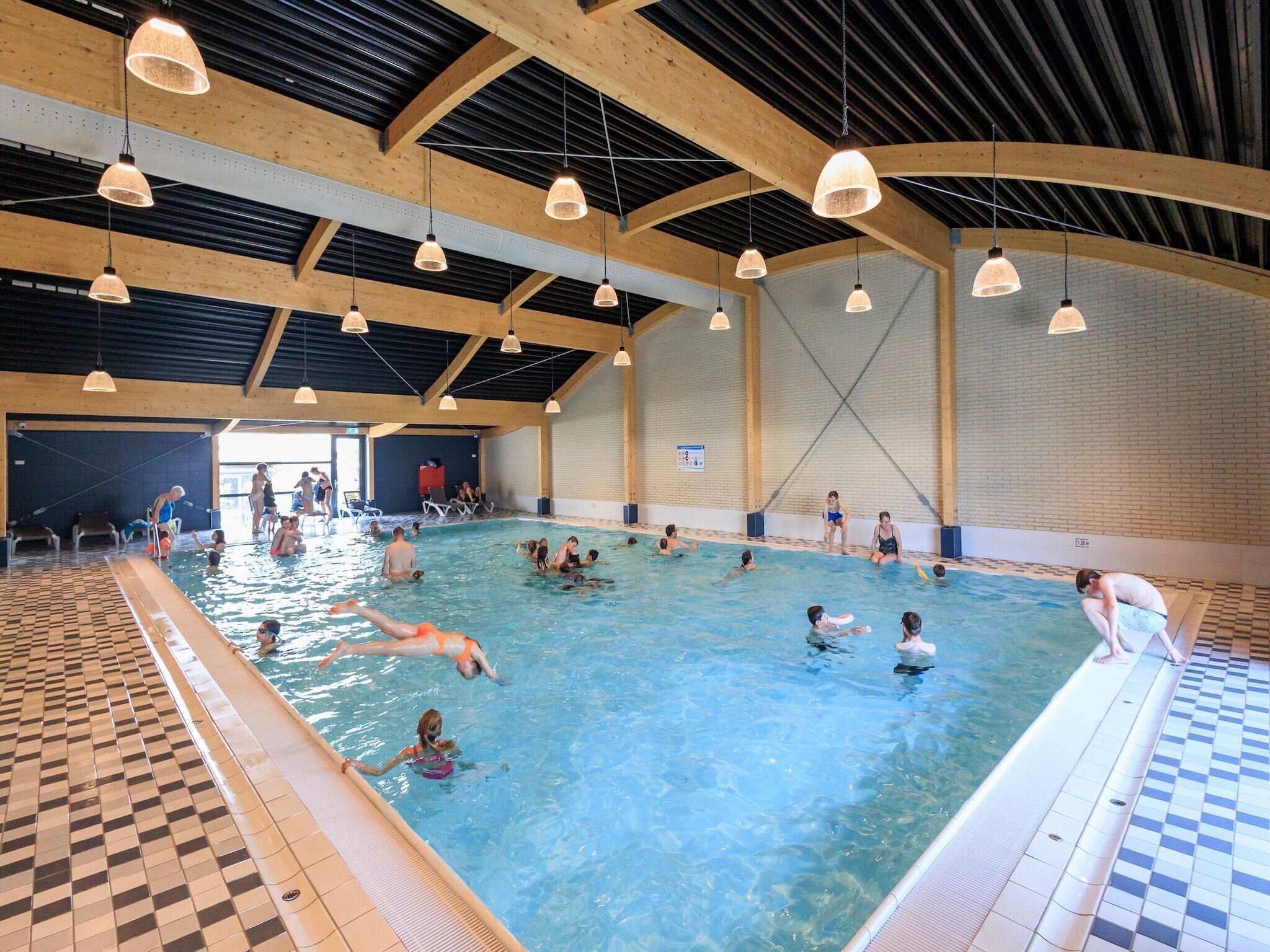 Una piscina interior con varias pistas de natación, vigas de madera y lámparas colgantes.