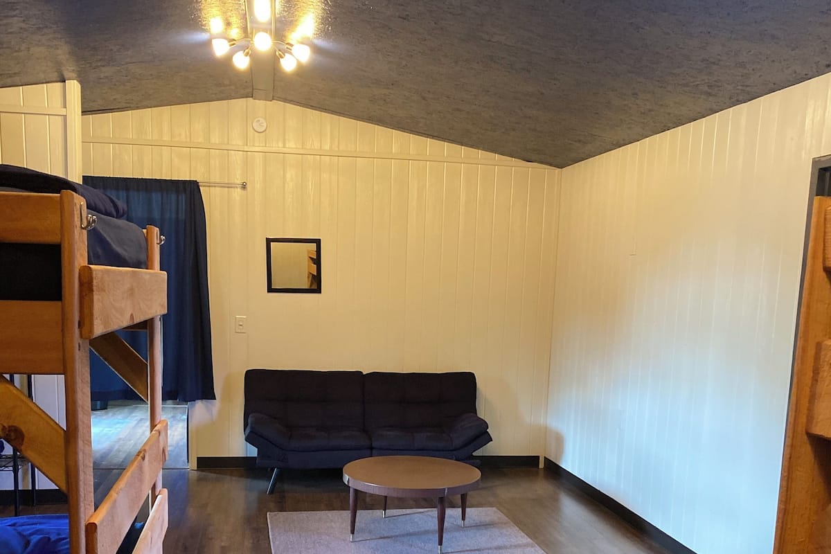 Ein Zimmer mit einem Etagenbett, einer Schlafcouch, einem kleinen runden Tisch und einem Spiegel an der Wand.