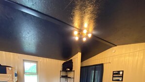 A room with a bunk bed, a sofa, a coffee table, a shelf with folded towels, and a window with a view of greenery. - Godspeed Events & Lodging (Port Matilda)