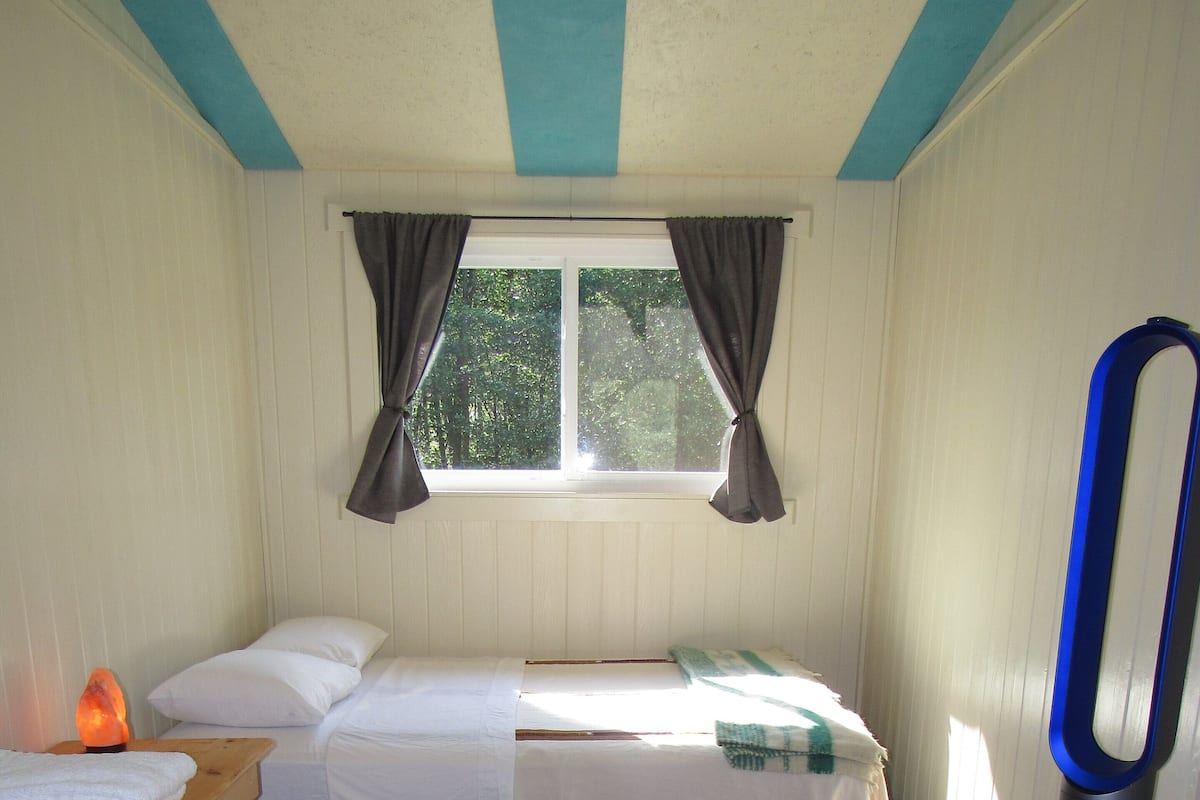 Ein kleiner, gemütlicher Raum mit einem Bett, einem Heizgerät, einem Tisch und einem Stuhl.