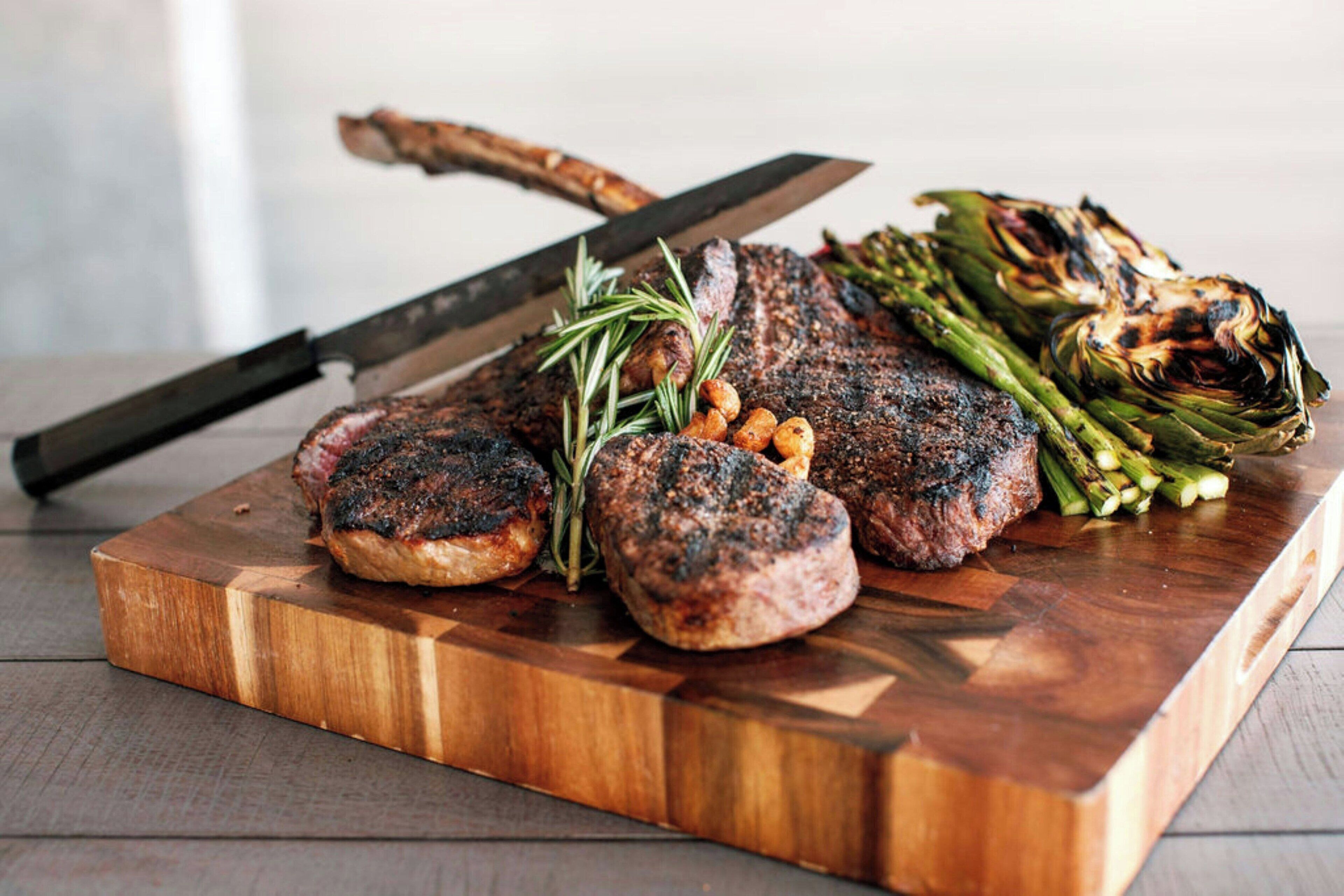 Een houten snijplank met gegrilde steak, asperges en champignons.