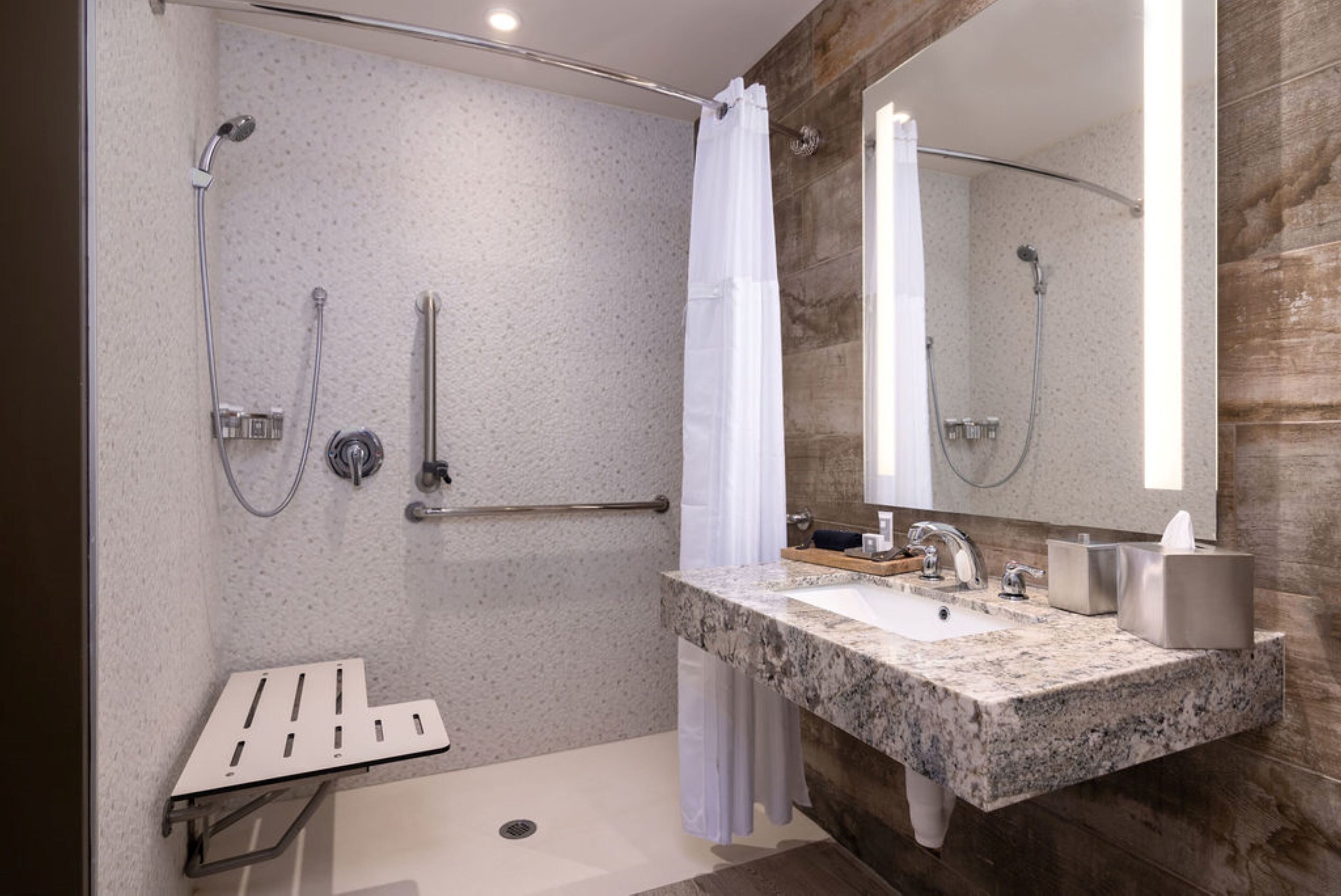 A modern bathroom with a granite sink, a handheld showerhead, a towel rack, and a mirror.