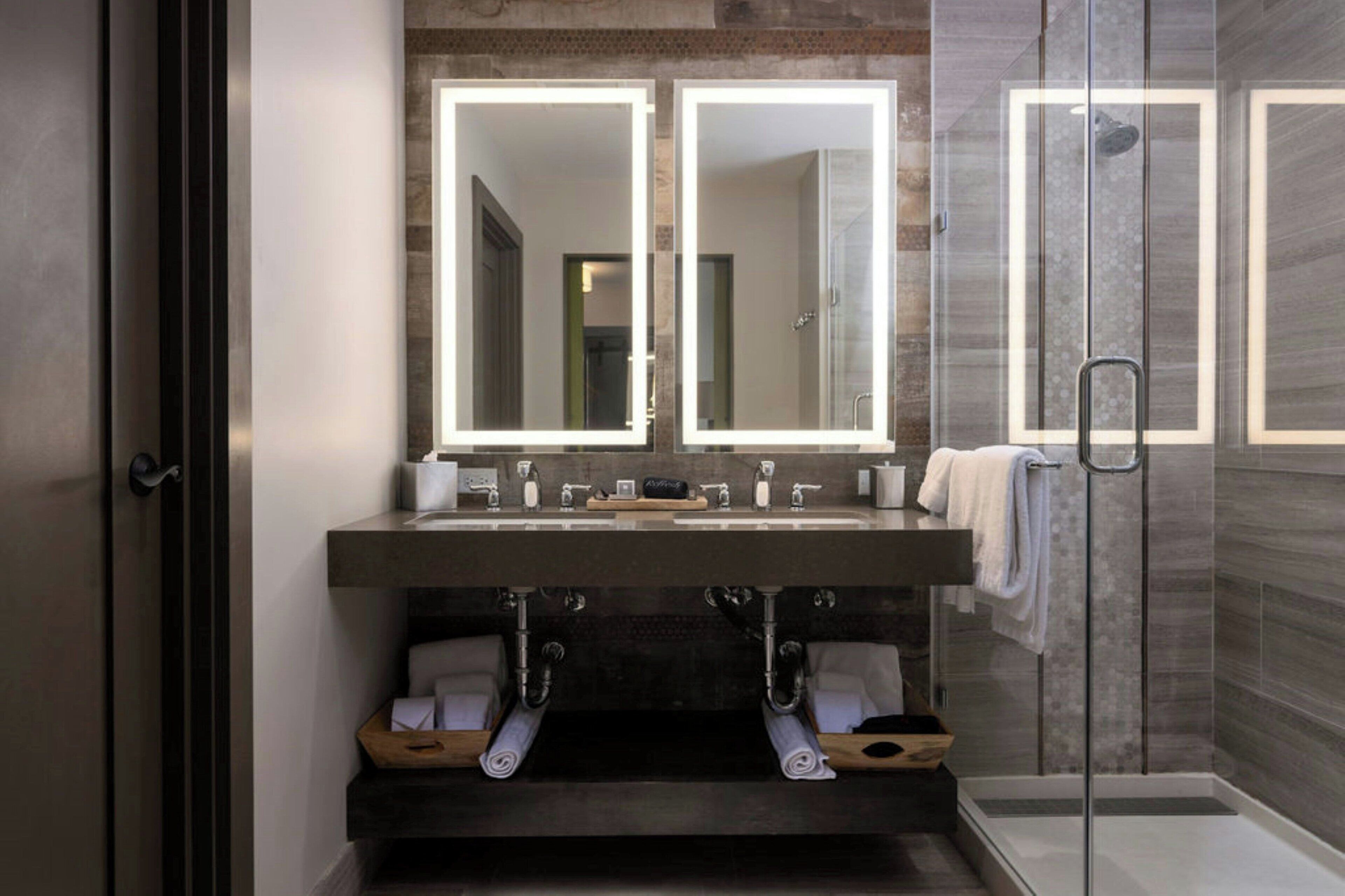 A modern bathroom with a double sink, two large mirrors, and a glass shower enclosure.