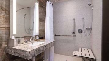 Un baño moderno con encimera de granito, un espejo grande, ducha con puerta de cristal y barra de apoyo.