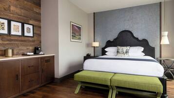 A bedroom with a wooden headboard, a green bench, a bed with white bedding, a nightstand, a lamp, and framed pictures on the wall.