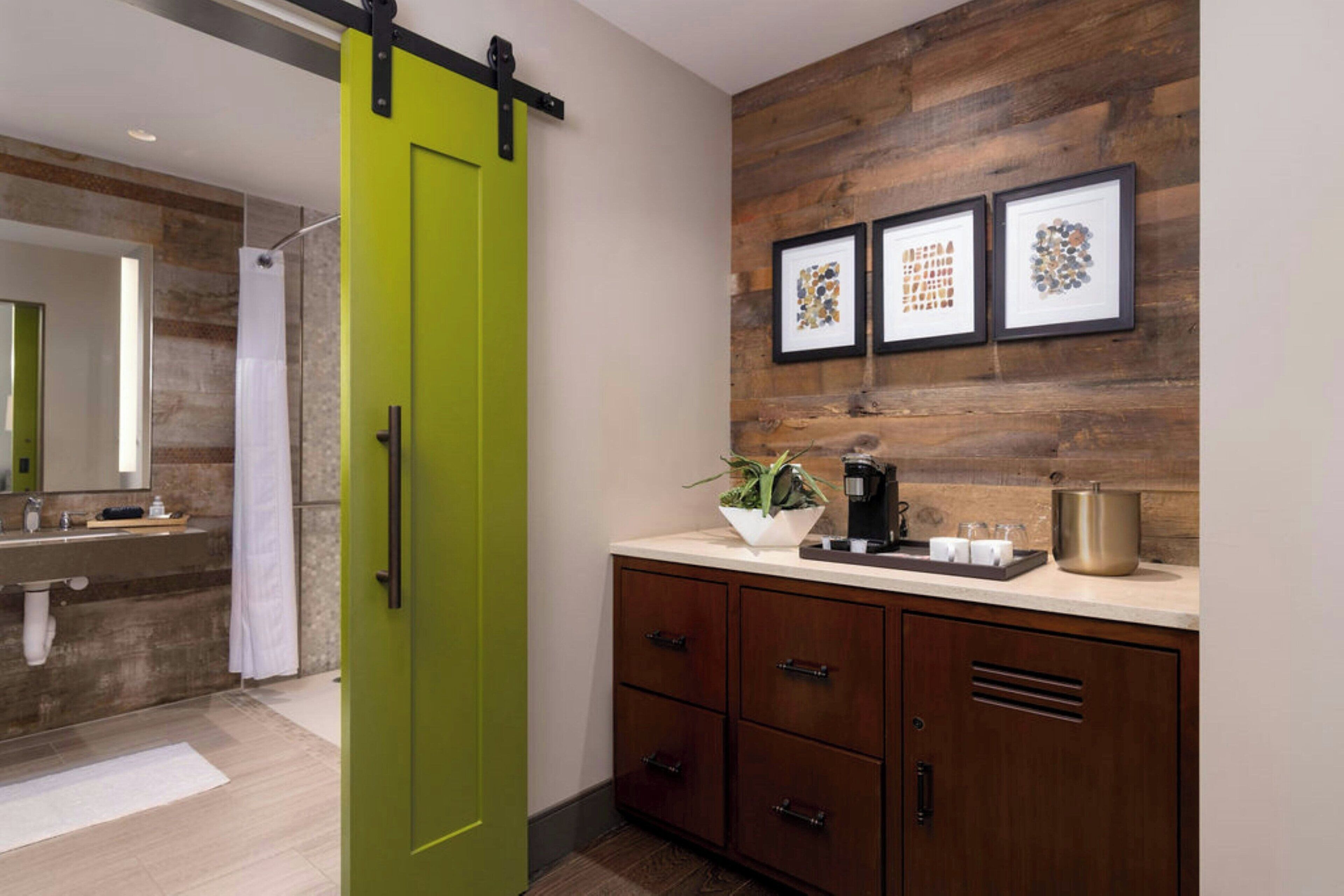 Une salle de bain moderne avec une porte verte, un lambris en bois, un lavabo avec un miroir et des œuvres d’art encadrées au-dessus du plan de travail.