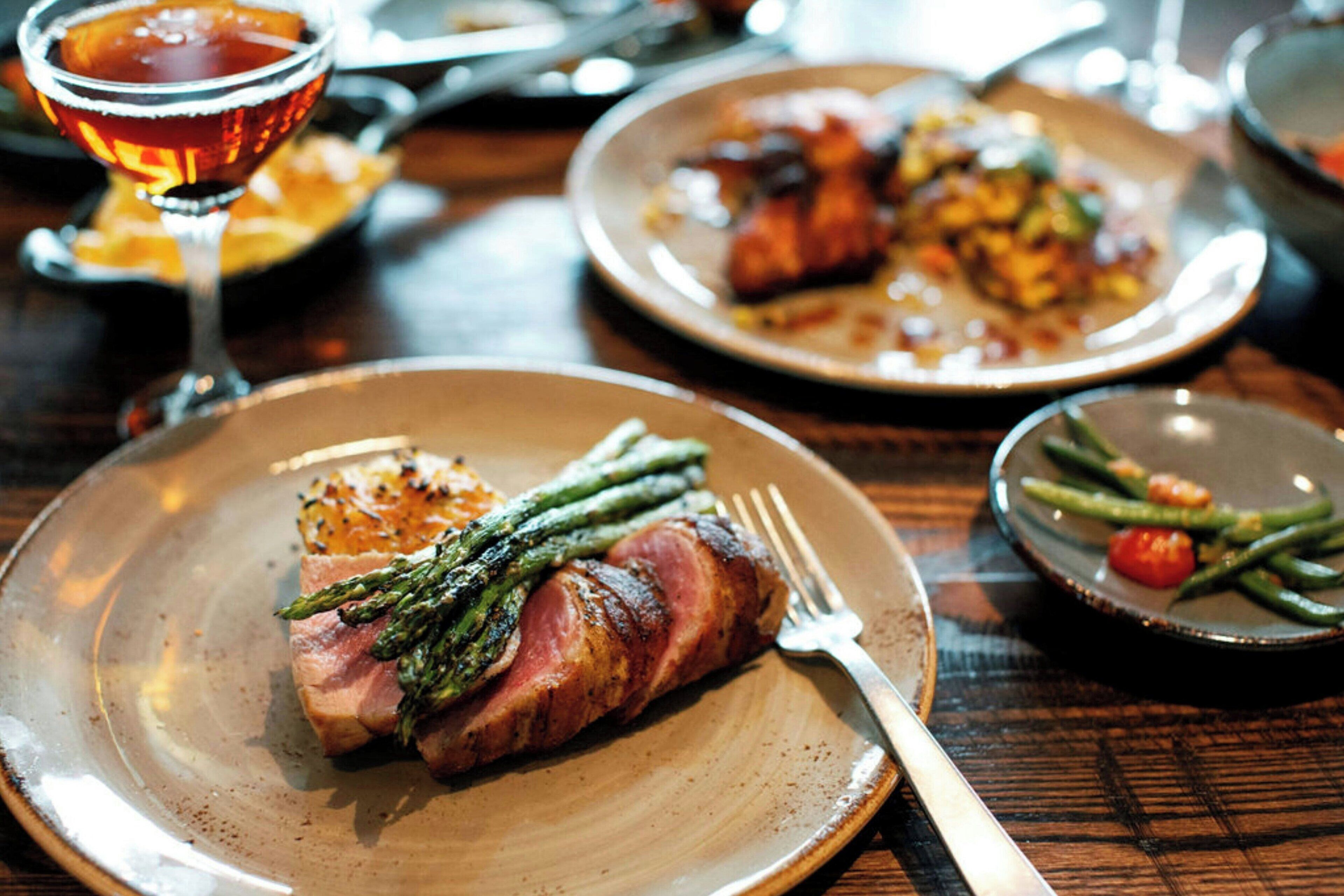 A dining table with plates of food, including a steak with asparagus, a glass of red wine, and a plate with green beans and tomatoes.