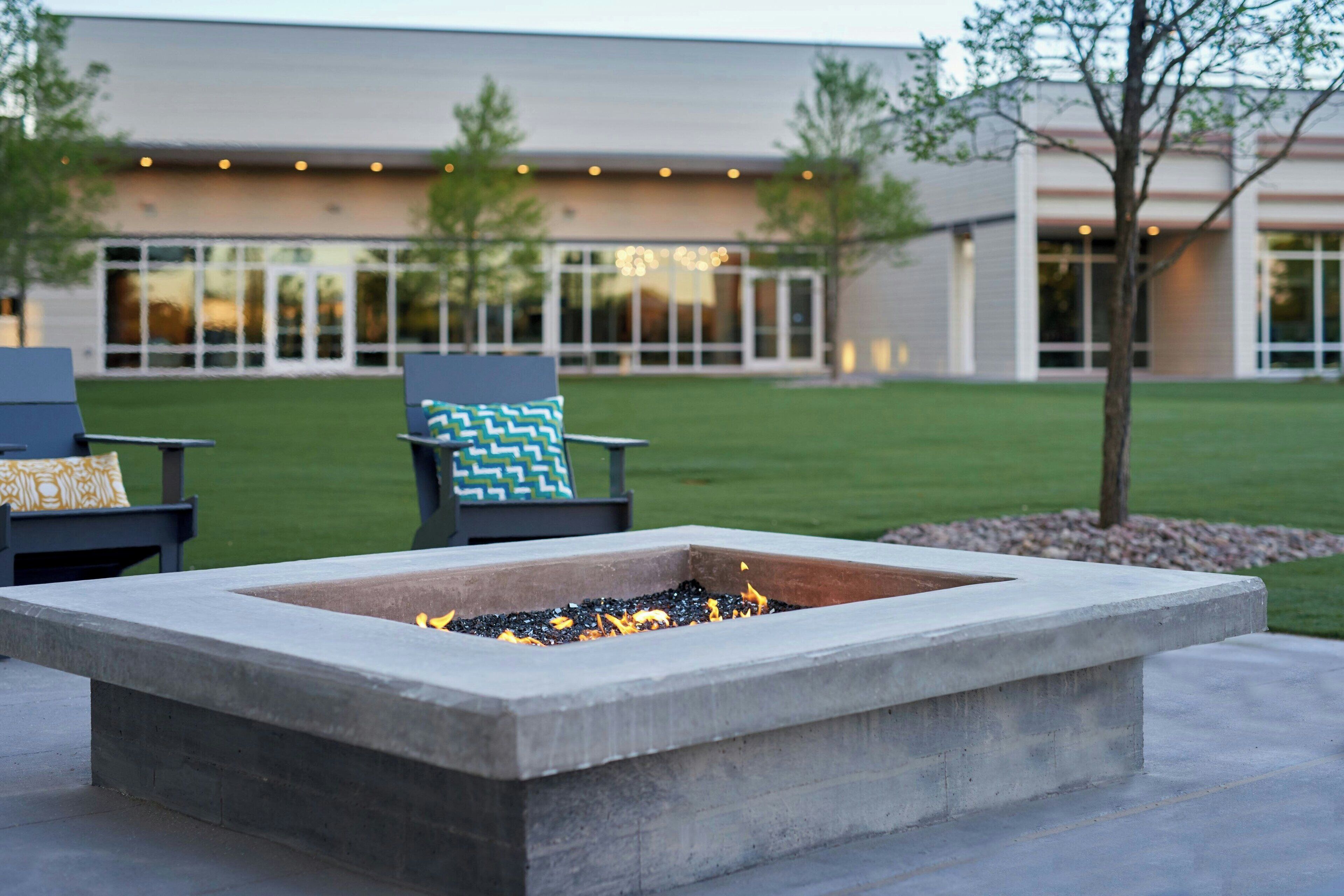 A concrete fire pit with a fire burning, surrounded by a patio area with two chairs and a cushion.