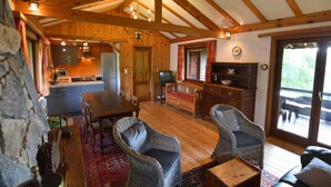 A cozy cabin interior with a wooden dining table, wicker chairs, a kitchen area, and a deck with outdoor seating.
