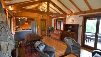 A cozy cabin interior with a wooden dining table, wicker chairs, a kitchen area, and a deck with outdoor seating.