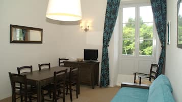 Ein Zimmer mit Esstisch, Stühlen, Fernseher, Sofa und einem Fenster mit Vorhängen.