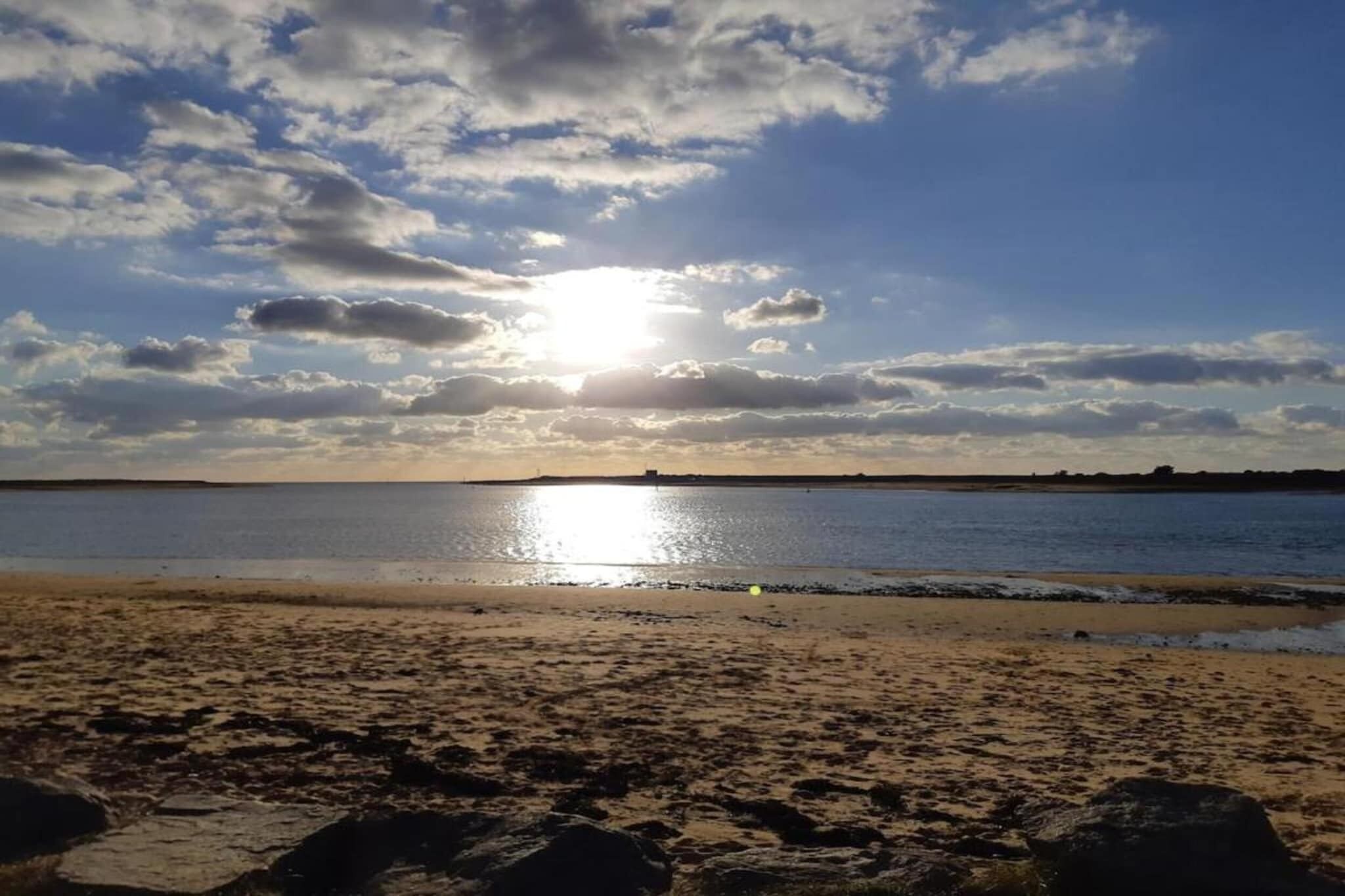 Una playa con un mar tranquilo, cielo despejado y un sol poniéndose o saliendo.