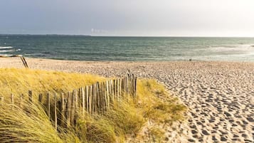 Une plage de sable avec une clôture en bois et de l’herbe au premier plan.