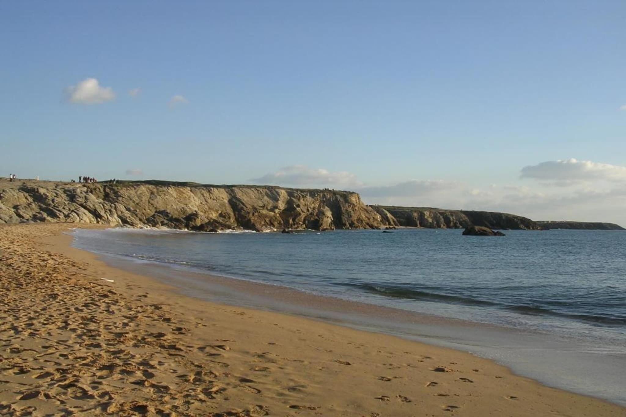 Una playa arenosa con un acantilado rocoso al fondo.