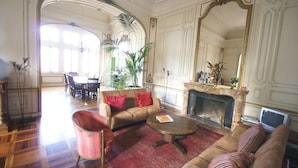 Un salon spacieux avec une cheminée, un grand miroir et un coin repas à l’arrière-plan.