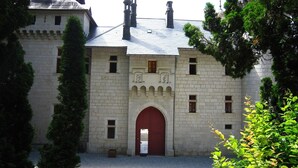 Un bâtiment historique en pierre, doté d’une arche rouge centrale, de nombreuses fenêtres et d’une façade symétrique.