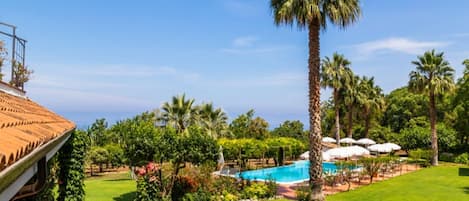 Un exuberante jardín con piscina, palmeras y sombrillas.