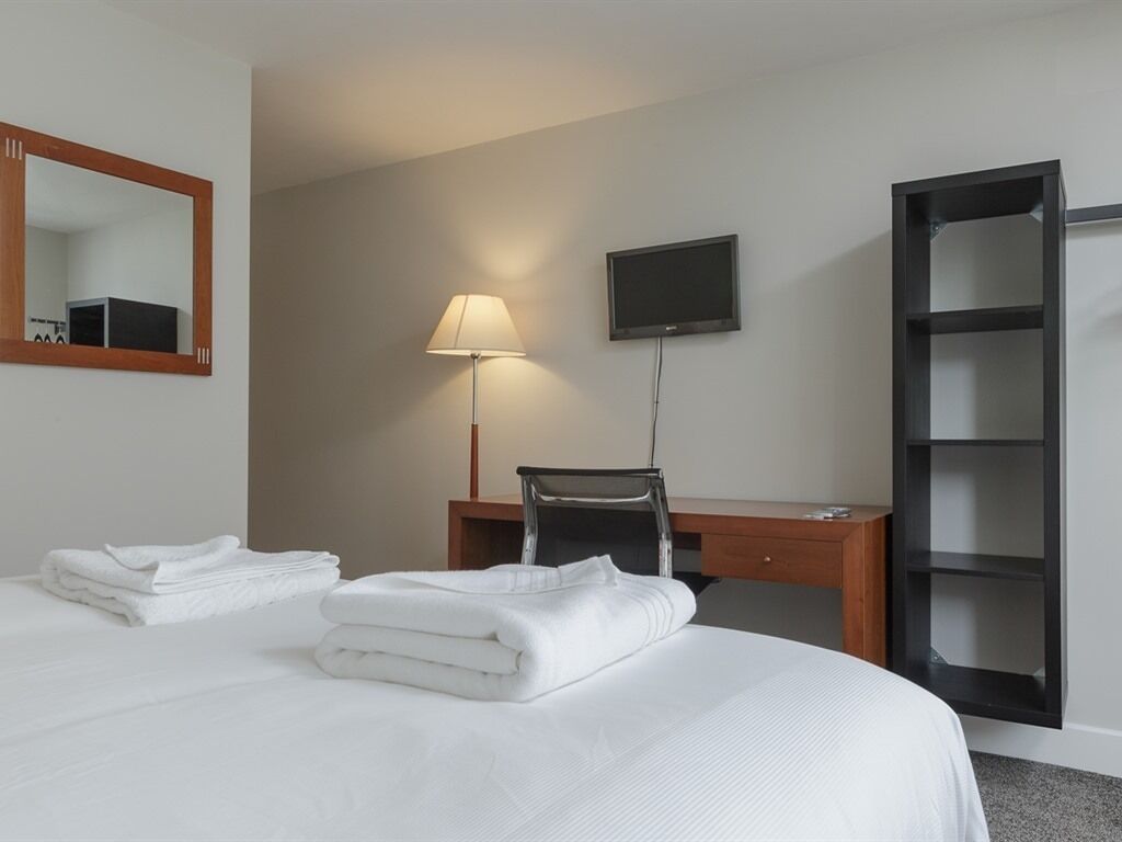 A hotel room with a bed, a desk, a chair, a TV, and a wardrobe.