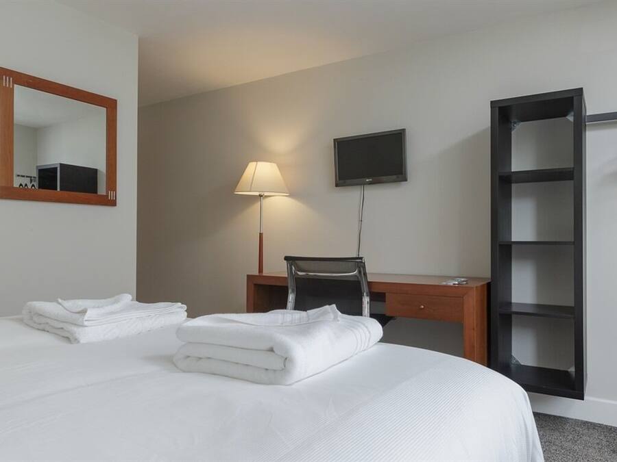 A hotel room with a bed, a desk, a chair, a TV, and a wardrobe.