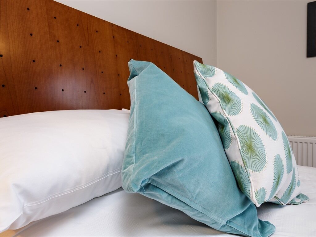 A bed with a wooden headboard, two pillows, and a wall with a picture frame.