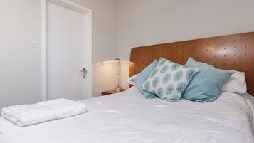 A neatly made bed with white linens and a folded white towel, a wooden headboard, and two bedside lamps.
