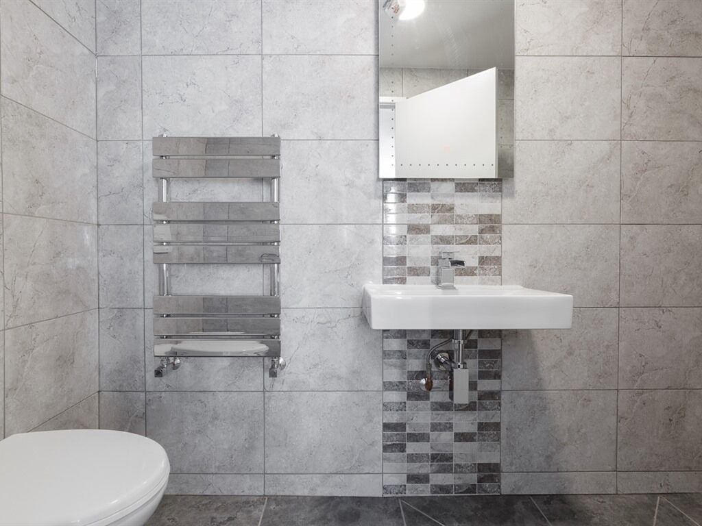 A bathroom with a toilet, a towel rack, a sink, and a mirror.