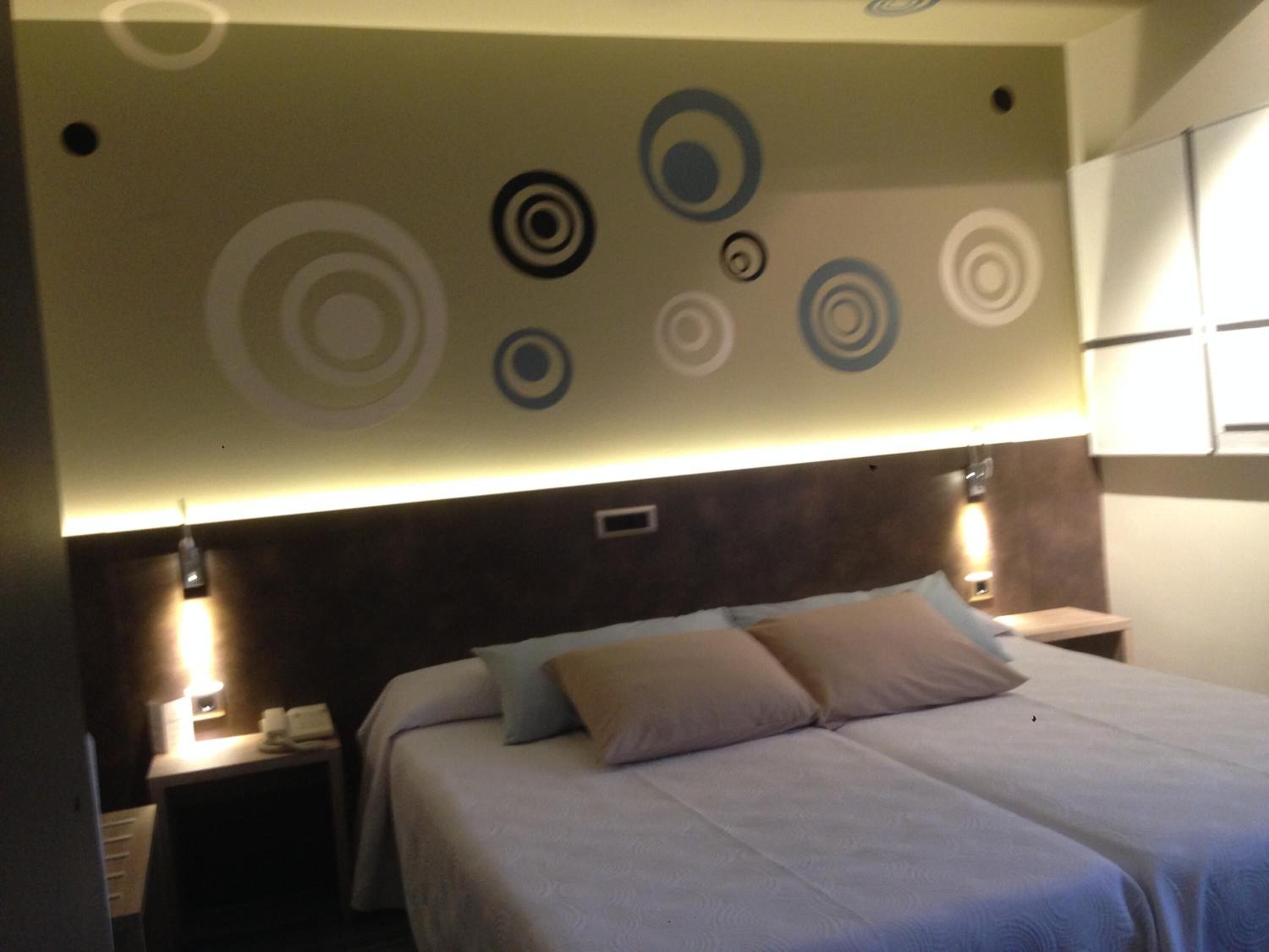 Une chambre d’hôtel avec un lit, des tables de chevet et un mur orné de motifs circulaires.