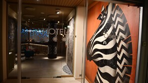 A hotel lobby with a modern design, featuring a large abstract wall art and a reception area with a patterned ceiling.
