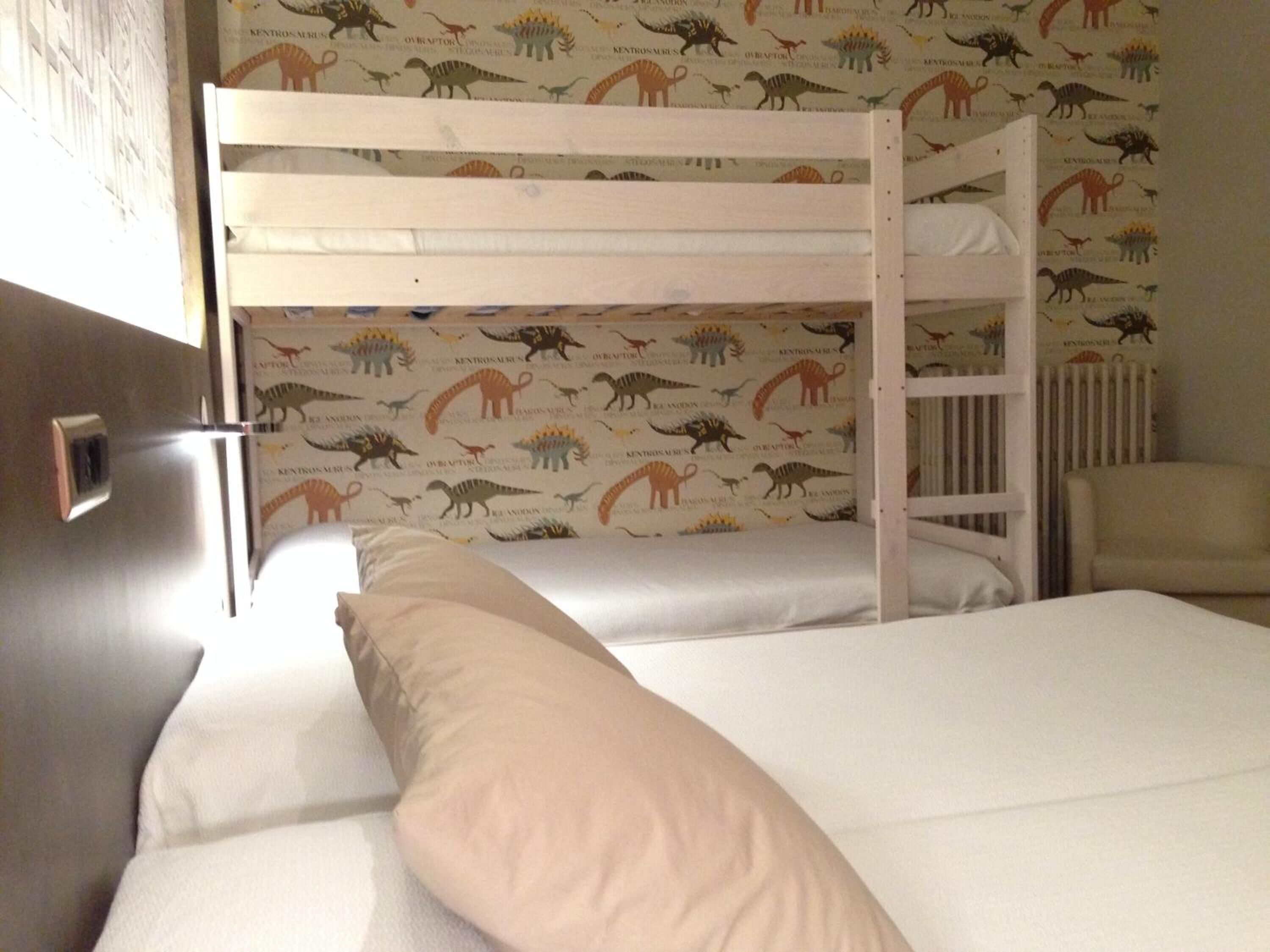 A bunk bed room with a dinosaur-themed wallpaper, a radiator, and a chair.