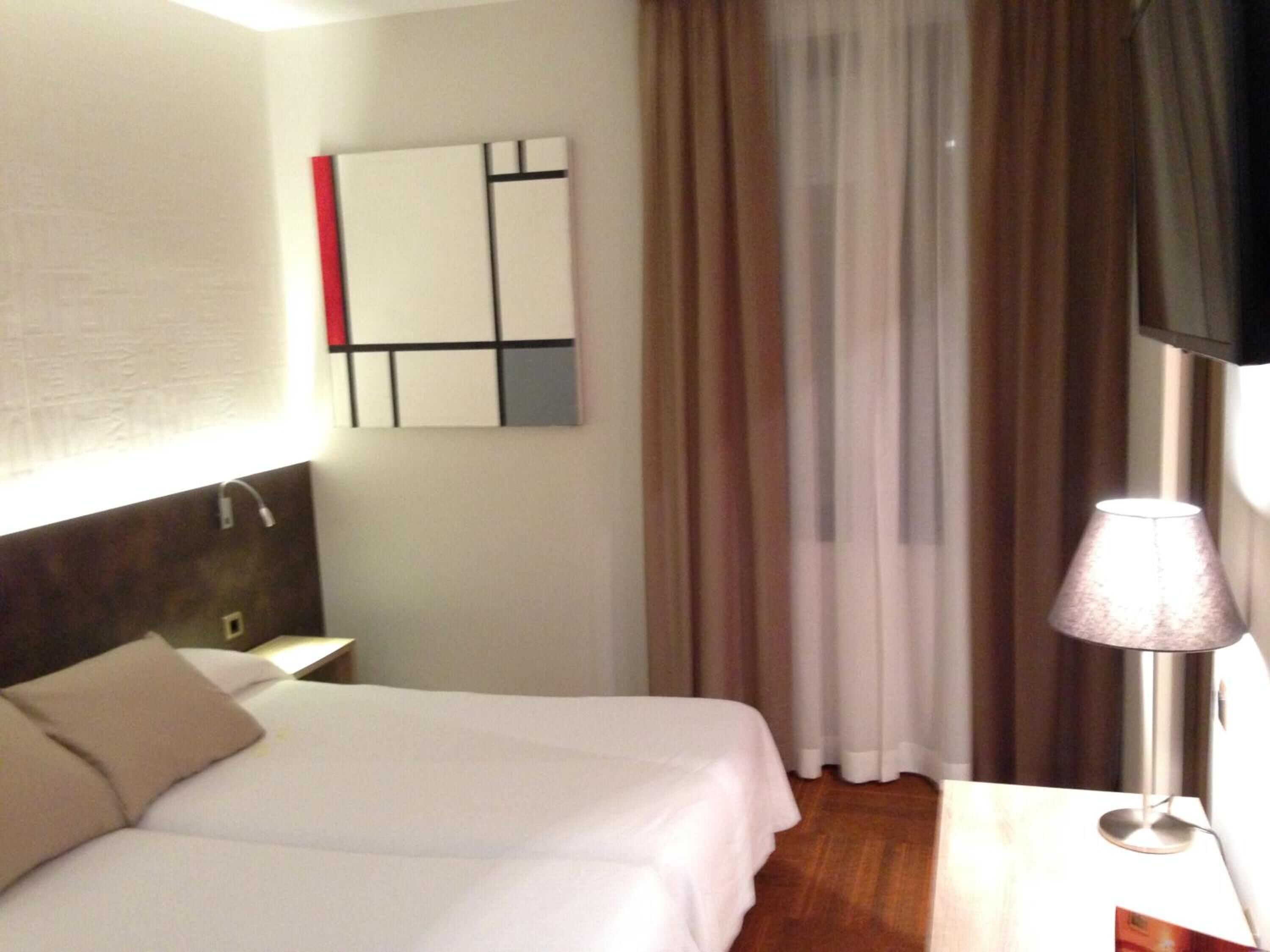 Ein Hotelzimmer mit einem Bett, einem Nachttisch, einer Lampe und einem an der Wand montierten Fernseher.