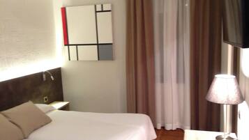 Ein Hotelzimmer mit einem Bett, einem Nachttisch, einer Lampe und einem an der Wand montierten Fernseher.