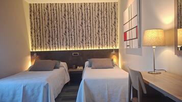 A hotel room with two beds, a desk, a chair, a lamp, and a wall with a birch tree pattern.