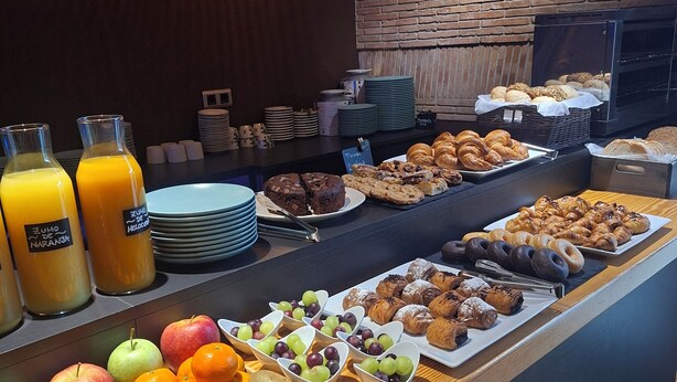 A breakfast buffet with fruits, pastries, and juice dispensers.