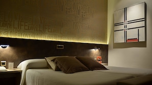 A hotel room with a bed, bedside tables, and a wall with a word cloud design.