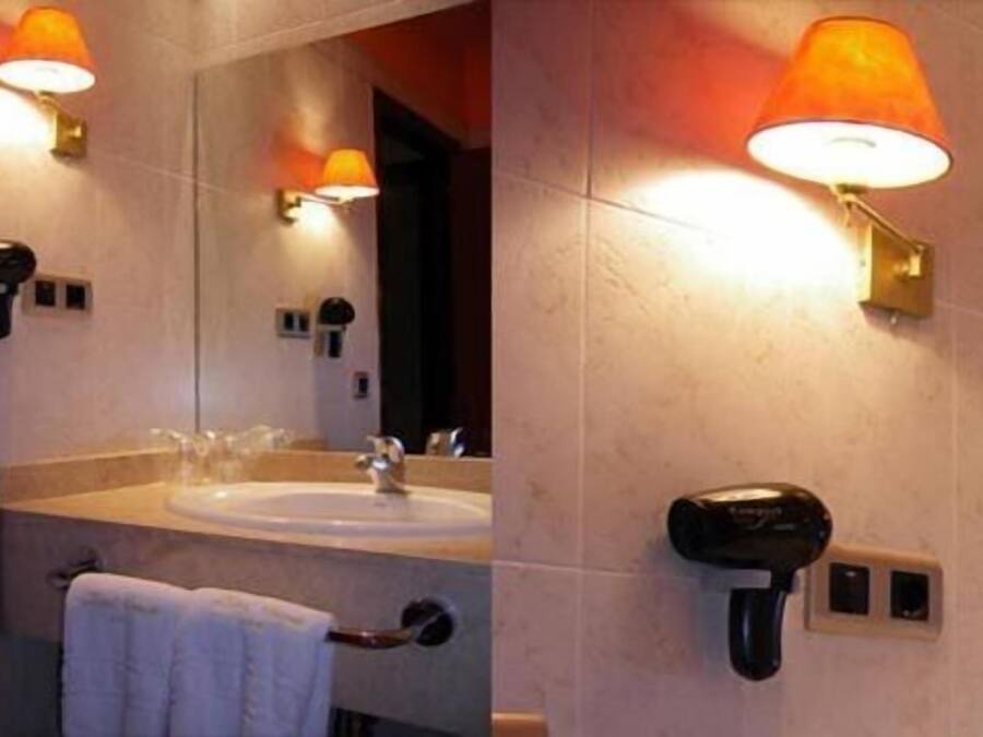 Une salle de bain équipée d’un lavabo, d’un miroir, d’un porte-serviettes et d’un sèche-cheveux fixé au mur.