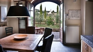 A rustic dining area with a wooden table and chairs, a pendant light, and a view of a garden through an open archway. - Hillside Escape in Vinci (Vinci - Florence)