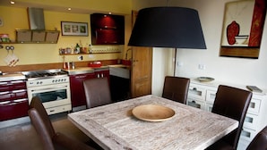 A dining area with a rustic wooden table, brown leather chairs, a black lamp, and a kitchen in the background. - Hillside Escape in Vinci (Vinci - Florence)