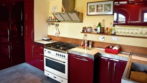A kitchen with a stove, oven, and red cabinets. There is a clock on the wall and a wine rack above the counter. - Hillside Escape in Vinci (Vinci - Florence)