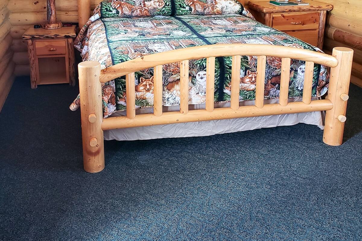 Una habitación de cabaña de madera con cama, mesita de noche, lámpara y un cuadro en la pared.