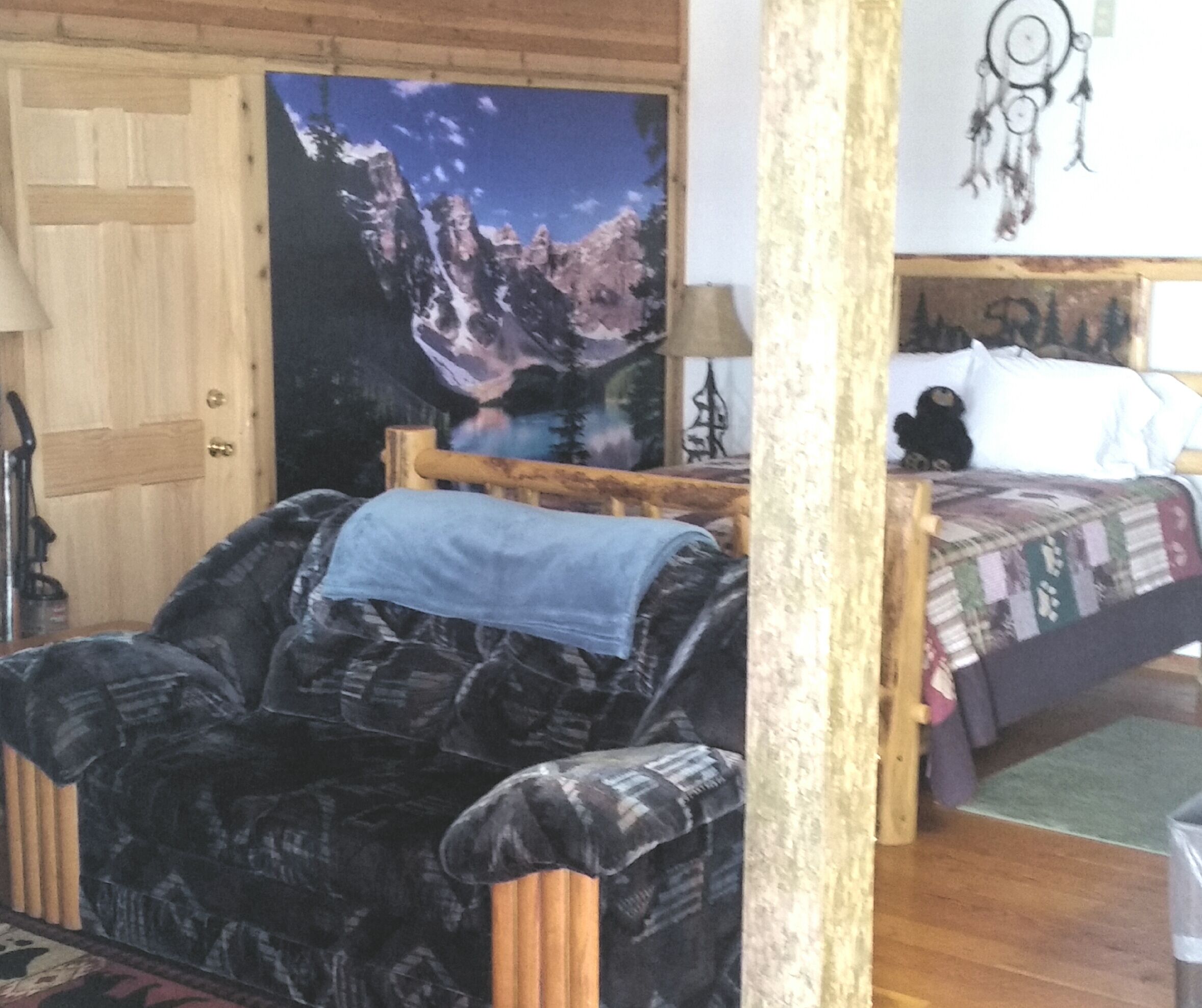 Ett rum med en säng, en stol, en trädörr och en stor målning som föreställer ett berglandskap.