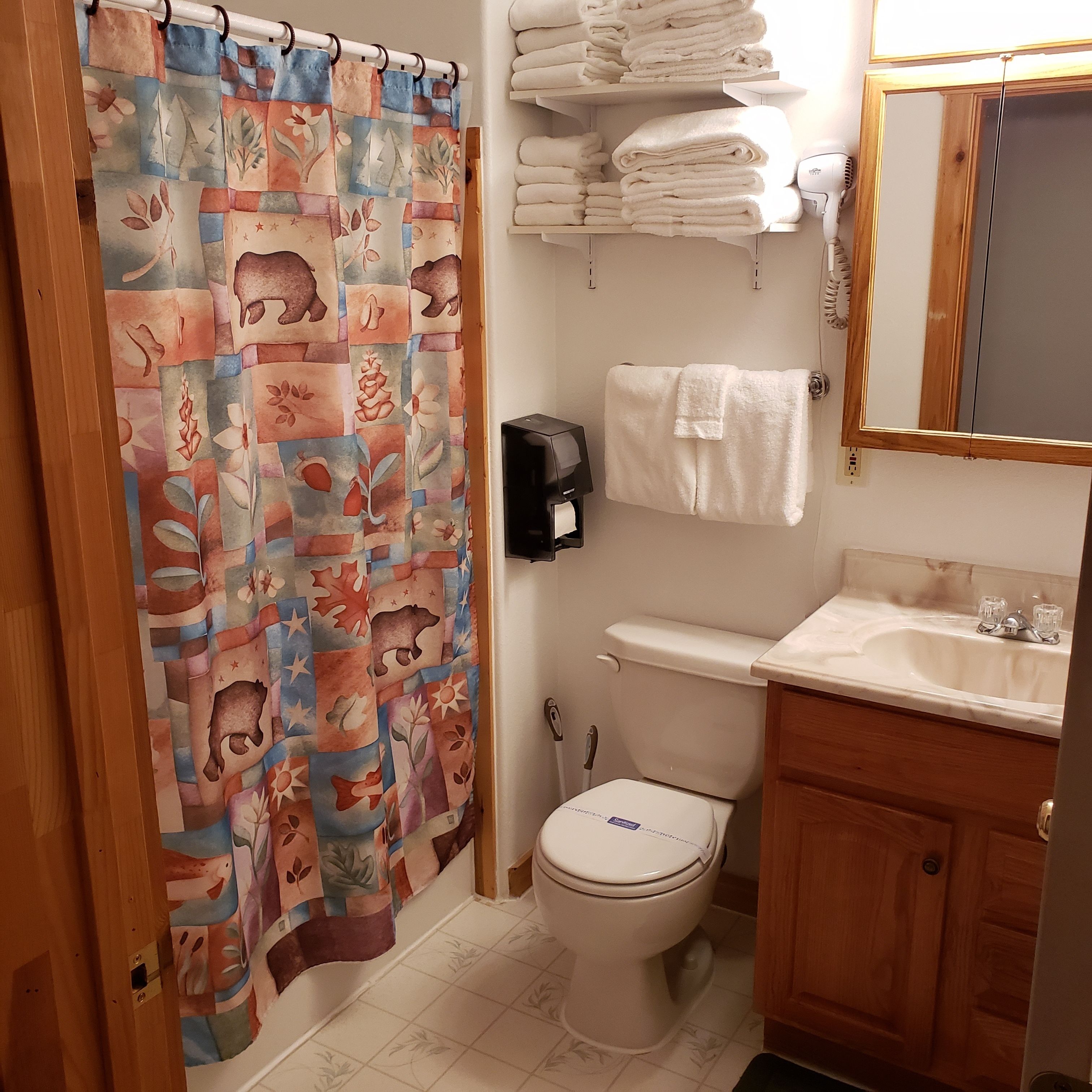 A bathroom with a patterned shower curtain, a toilet, a sink with a mirror, and neatly stacked towels.