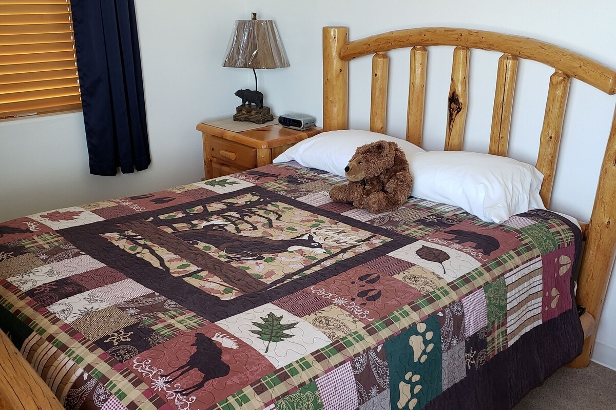 Un lit en bois avec une courtepointe, une lampe de chevet et une horloge posée sur une table de chevet en bois.