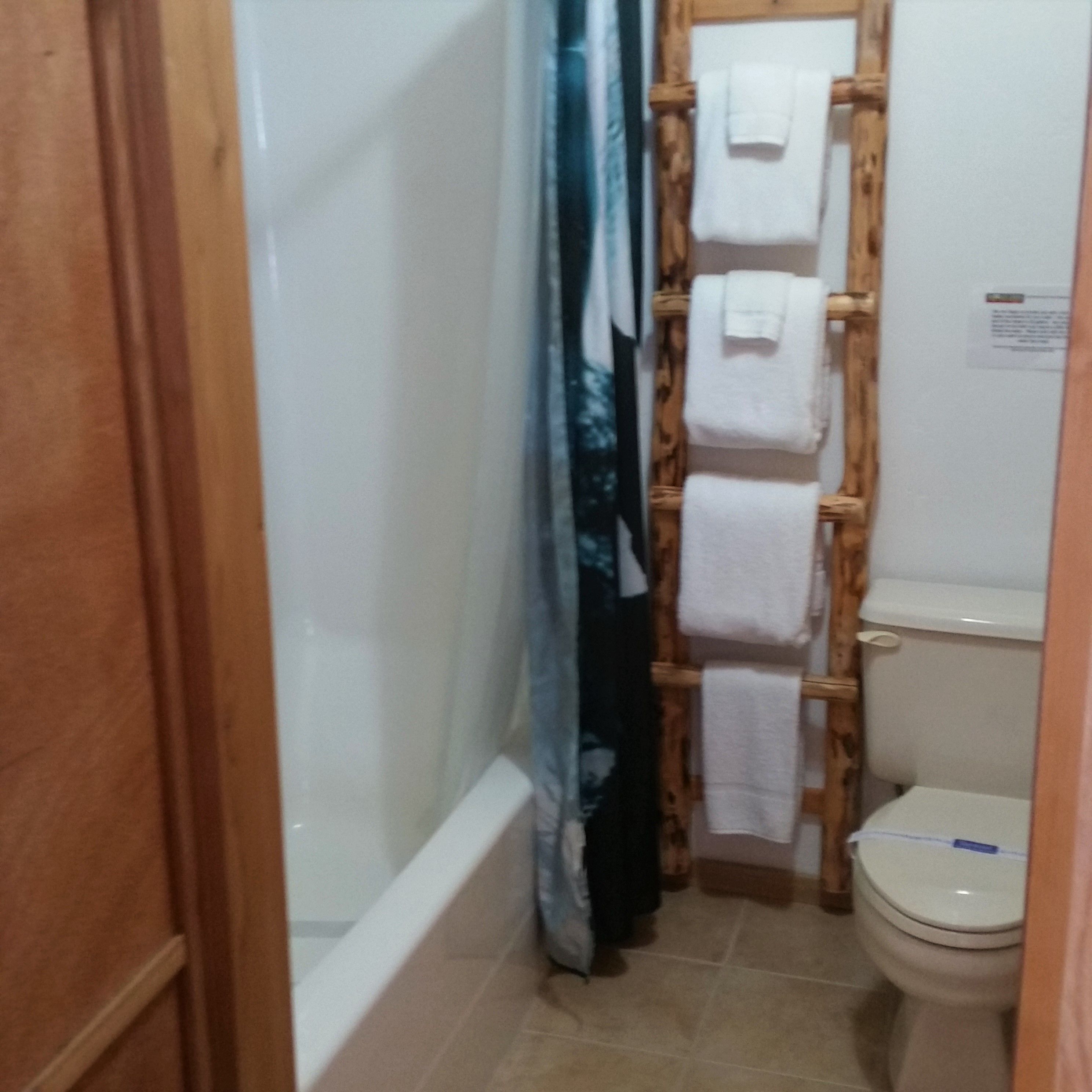 Un baño con inodoro, un perchero de madera y cortina de ducha.