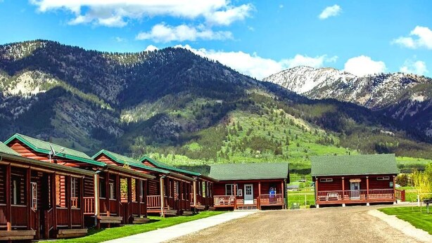 A row of log cabins with green roofs, set against a backdrop of mountains and a clear sky. - Wolf Den Log Cabin Motel and RV Park (Etna)