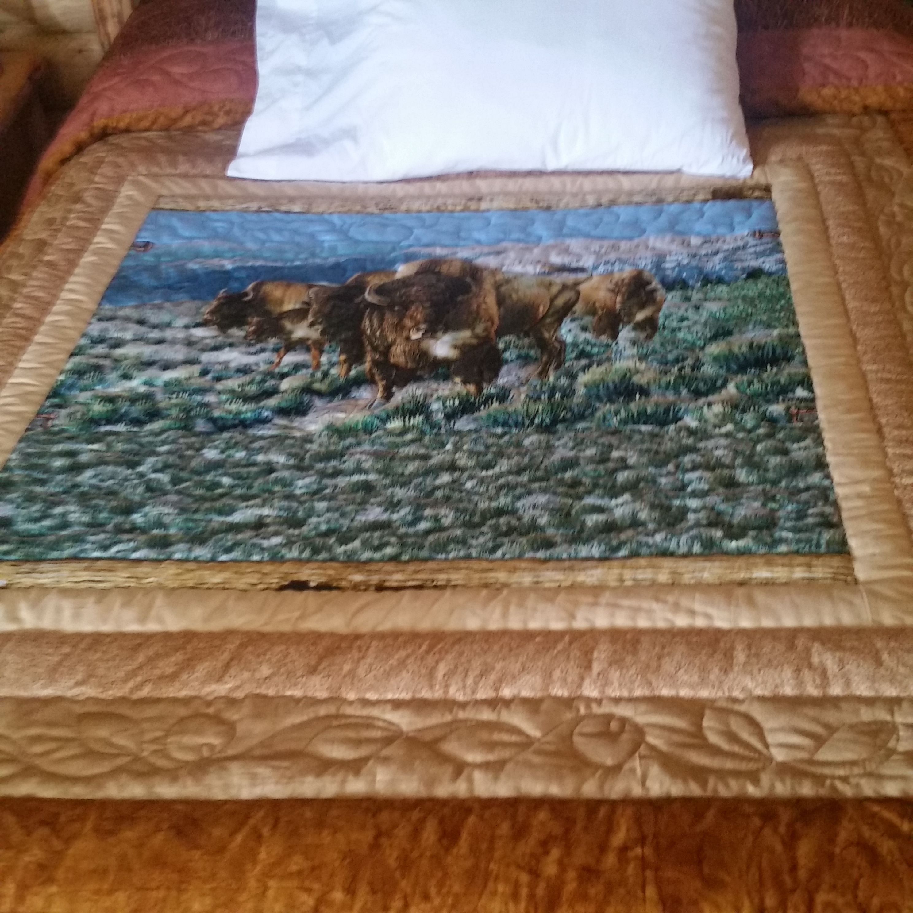 A bed with a painting of bison on a textured blanket.