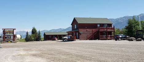 A rustic lodge with a prominent wooden structure, a gravel parking area, and a mountainous backdrop.
