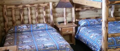 A rustic room with wooden bunk beds, a small bedside table with a lamp, and a framed picture on the wall.