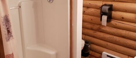 Un baño con una bañera blanca, un dispensador de jabón Gojo, un inodoro y una pared de troncos de madera.